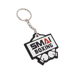 The SMAI Boxing Keyring - Rubber by SMAI features a rectangular tag with "SMA BOXING," a red "A," and two boxing gloves. This bold black, white, and red keyring is the perfect accessory for boxing fans.