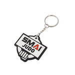 The SMAI Judo Keyring - Rubber features a metal ring and a rubber tag with "SMAI JUDO" printed in bold black and red on a white, black-edged background.
