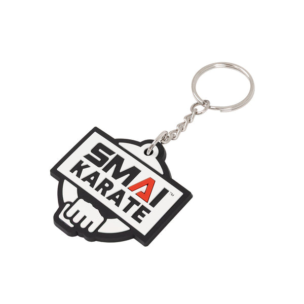 The SMAI Karate Keyring - Rubber features the rectangular "SMAI KARATE" logo in black and white with a red "A," a stylized fist outline in the background, and comes attached to a chain and keyring.