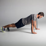 An individual in athletic wear is performing a push-up using the SMAI Rubber Resistance Band - 50lb under their arms on a smooth, light-colored floor, concentrating on maintaining proper form in a plank position.