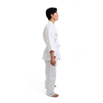 A person in profile stands barefoot, wearing the SMAI Shinkyokushinkai Uniform - 8oz Student Gi, including a belt, against a plain white background.