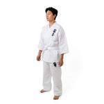 A person stands barefoot on a white background, wearing the SMAI Shinkyokushinkai Uniform - 8oz Student Gi featuring Kanji embroidery on the chest. The medium-weight fabric drapes elegantly as they rest their hands at their sides, gazing thoughtfully to the side.