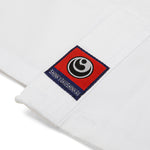 Close-up of the SMAI Kin Kyokushin Uniform (8oz Student Gi) shows a white karate gi with a rectangular patch featuring a black and white circular logo on red. "SHINKYOKUSHINKAI" text below honors its martial arts heritage.