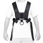 A person wears the SMAI Tower Gym Sled 3.0 with sled harness—featuring wide black straps and a front metal ring—over a white t-shirt and light shorts, preparing for sprint training.