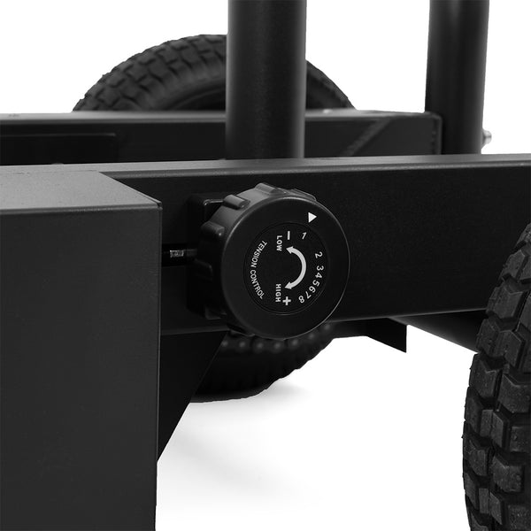 Close-up of a black adjustment knob with a numbered dial and arrows on the SMAI All Terrain Resistance Sled's wheeled metal frame. Two large rubber tires are partially visible in the background.