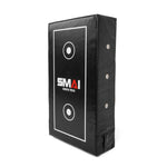 The SMAI Kick Shield - Shoc Tec Straight is a rectangular black shield with white target markings, metal side rivets, impact-absorbing foam, and the "SMAI SHOCK TECH" logo printed on the front.