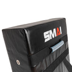 The SMAI Kick Shield - Shoc Tec Straight is a black rectangular pad with a handle and straps, made from lightweight materials and impact-absorbing foam for safe martial arts training. "SMAI" is printed on the surface.