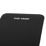 A close-up of the SMAI "The Yard - Workout Mat," a black mat with "THE YARD" in white on one corner. It features a textured, grippy surface and rounded edges.