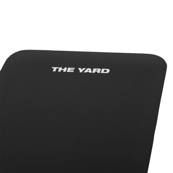A close-up of the SMAI "The Yard - Workout Mat," a black mat with "THE YARD" in white on one corner. It features a textured, grippy surface and rounded edges.