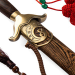 Close-up of the SMAI Tai Chi Sword Brass Fitting Ying Yang, featuring an ornate brass guard with engraved Yin-Yang symbol, spring steel blade, dark wooden scabbard, and decorative red and brown tassels.