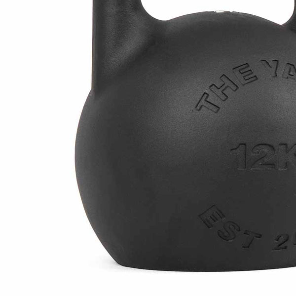 A close-up of the SMAI The Yard - Competition Steel Kettlebell 36kg, featuring custom branding and embossed details on its black surface.