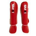 The Essentials Muay Thai Shin Instep Guard by SMAI is shown in red synthetic leather with white trim and the SMAI logo on the shin, displayed from the front against a white background.