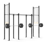 The gym setup features the Rig - 4 Squat Cell with Bridge by No Sync To Channel Engine, constructed from durable steel tubing and equipped with loaded barbells and hanging gymnastic rings. This commercial equipment is displayed against a plain white background, accentuating its robust modular design.