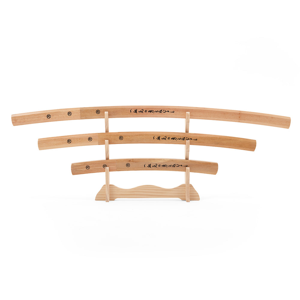 The SMAI Shirasaya 3pc Sword & Stand features three minimalist wooden Japanese swords of varying lengths with black kanji, displayed horizontally on a wooden stand against a white background.