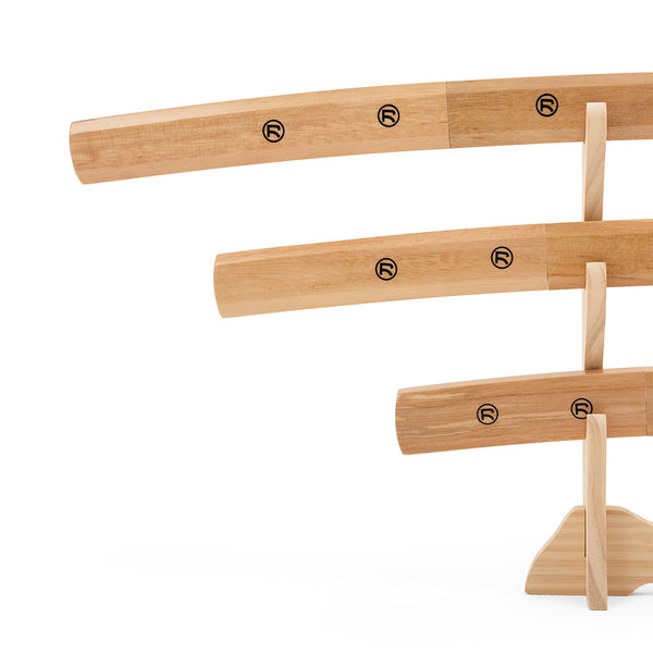 The SMAI Shirasaya 3pc Sword & Stand set features three wooden practice swords, each with a unique circular logo, displayed at varying heights on a Japanese stand against a plain white background.