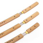 The SMAI Shirasaya 3pc Sword & Stand features three sleek swords with wooden handles and exposed blades, arranged parallel on a white background. Japanese characters on the handles recall a minimalist, refined katana display.
