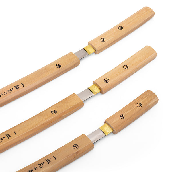 The SMAI Shirasaya 3pc Sword & Stand features three sleek swords with wooden handles and exposed blades, arranged parallel on a white background. Japanese characters on the handles recall a minimalist, refined katana display.