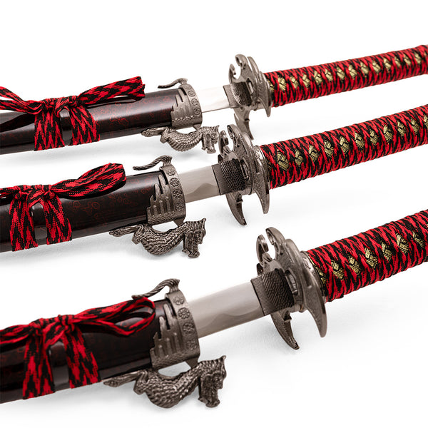 The Daisho - 3pc Set with Stand - Molten Dragon by SMAI, featuring ornate hilts, red and black braided handles, and dragon-shaped accents, is displayed diagonally on a white background.