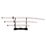 The SMAI White Samurai 3pc Sword & Stand includes a katana, wakizashi, and tanto, each with decorative patterns on the scabbards and handles, displayed horizontally on a sleek black stand.