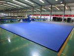 A large factory space features a SMAI Dollamur Flexi Connect Gym Flooring Roll in royal blue covering part of the floor, surrounded by equipment and illuminated by bright lights, showcasing advanced athletic foam technology.
