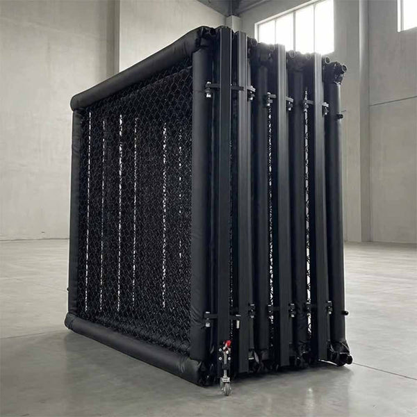 The SMAI MMA Cage - 5m Fold Away, a black portable cage with mesh panels and wheels, is set up in a spacious concrete-walled room featuring tall windows.
