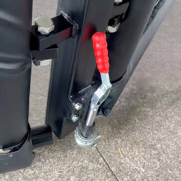 A close-up of the SMAI MMA Cage - 5m Fold Away shows a metal latch with a red, ribbed handle on its black folding frame, positioned on concrete, highlighting its space-saving design.