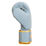The SMAI Gold Series Boxing Glove in Light Blue/Gold stands upright against a white background, crafted for superior wrist support and enhanced shock protection.