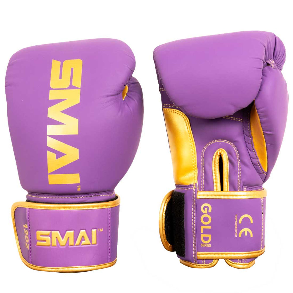 Introducing the SMAI Gold Series Boxing Glove - Purple/Gold: This pair features striking purple and gold colors with the "SMAI" logo prominently displayed. One glove presents the front view, while the other highlights the palm side and a wrist strap marked "GOLD SERIES." Engineered for both style and performance, these gloves deliver superior wrist support and shock protection for every training session.
