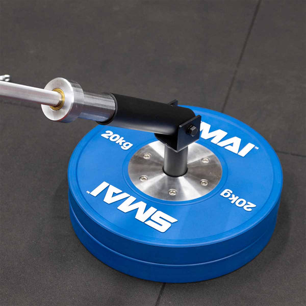 The SMAI The Yard - Drop In Landmine / Core Trainer fits into a 20kg blue weight plate on the gym floor, securing a barbell for rotational and pressing exercises—ideal for effective core barbell workouts.