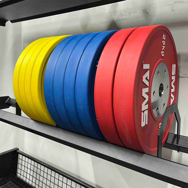The SMAI Bumper Plate Toaster Storage Shelf - Vanta Series neatly holds colorful yellow, blue, and red "25 kg" SMAI bumper plates, providing organized and efficient storage against the gym wall.